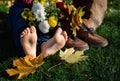 bare feet of child lying on grass next to a bouquet of autumn leaves in brown shoes on a warm sunny autumn day