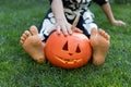 bare feet of a child sitting on the grass, between his legs a carved Halloween orange pumpkin Royalty Free Stock Photo