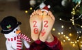 bare feet of a child on which the numbers 2024 are written, luminous garlands, a toy snowman