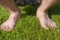 Bare feet of man in shorts squatted on lush grass on lawn in summer