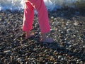 Bare feet in pink pants walking on the pebbles washed by the sea surf