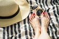 bare feet with red pedicure on striped blanket, sun hat and sunglasses beside