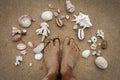 Bare feet on sandy beach with beautiful seashells around Royalty Free Stock Photo