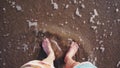 Bare feet sink and squish into the wet brown sand at the edge of coming waves