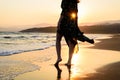 Bare feet woman in green dress on the beach before the orange sunset, silhouette with rays