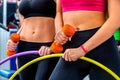 Bare female belly with dumbbells and hoop at gym