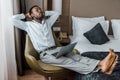 Barefoot african american man with closed eyes relaxing in armchair with laptop