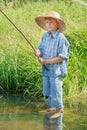 Barefoot angler boy fishing standing in transparent freshwater pond Royalty Free Stock Photo