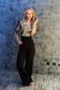 Barefoot blonde with a haircut in black trousers and a golden shirt poses against a gray wall Royalty Free Stock Photo