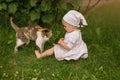 A barefoot child plays with a cat in the village near a grape bush