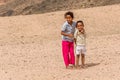 Barefoot children in tattered clothes in a Bedouin village, posing for photos.