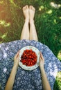 Barefoot girl is sitting on the grass in blue vintage dress. Woman is holding plate with home strawberries. Rustic summer fruit Royalty Free Stock Photo