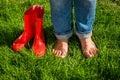 Barefoot girl standing next red garden gumboots on grass Royalty Free Stock Photo