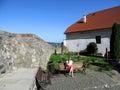 Barefoot girl-tourist in sunglasses sits on a bench in the courtyard of the medieval castle Palanok Mukachevo, Ukraine. Adult Royalty Free Stock Photo