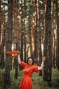 Barefoot happy young woman in red dress with hand raised dancing in pine forest at summer day. Royalty Free Stock Photo