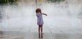 Barefoot little girl standing playing in a fountain in town