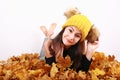 Brunette girl in yellow cap with bobbles lying on autumn leaves Royalty Free Stock Photo