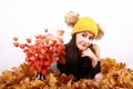 Brunette girl in cap with bobbles lying on autumn leaves by flowers Royalty Free Stock Photo