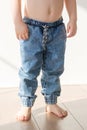 Barefoot toddler boy in elasticated jeans is standing on the floor