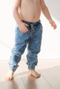 Barefoot toddler boy in elasticated jeans is standing on the floor