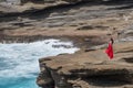 A barefoot woman in a bright red dress standing near the ocean cliff on Oahu