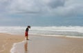 Barefoot woman in hat and dress looks down at her mud covered feet on beach on the Gold Coast of Queensland Australia 02-23-2015