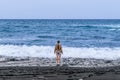 Barefoot woman in shorts and a beige sweater stands on black volcanic sand Royalty Free Stock Photo