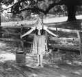 Barefoot woman in a tied bodice dress carrying water buckets on shoulder poles