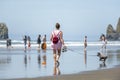 A barefoot woman walking a small playful terrier dog on the shore of the Northwest Pacific Ocean together with other vacationers