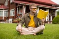 Barefoot young man wearing yellow glasses sitting on green grass reading book Royalty Free Stock Photo