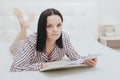 Barefoot young teenage girl looking at the camera lying on her bed reading a book Royalty Free Stock Photo