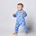 Barefooted blond baby boy toddler in blue fleece jumpsuit with stars stands steadily with his legs spread wide.