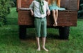 A barefooted girl in a green dress is sitting in an old caravan, and beside her, barefoot, on the grass, stands a guy in a white s Royalty Free Stock Photo