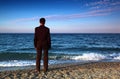 Barefooted man in suit stands back on stone coast