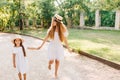 Barefooted slim young woman running in the yard, holding hands with daughter in trendy straw hat. Outdoor portrait of Royalty Free Stock Photo