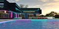 Barely noticeable waves on the surface of the pool, reflecting the neon illumination of the facade of a chic modern mansion built