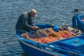 Fisherman with a hat repairing with a big needle a fishing net on an old blue wooden fishing boat Royalty Free Stock Photo
