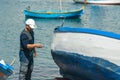 Fisherman repairing and painting an old wooden fishing boat at the port quay