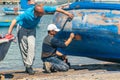 Fishermen repairing and painting an old wooden fishing boat at the port quay