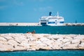 Tanned bather sunbathing on the breakwater with pier, cruise ship, blue sky, blue sea