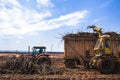 A tractor with a lifting claw loading a truck with sugar cane