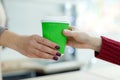 Barista in apron is giving hot coffee in green takeaway paper cup to customer. Coffee take away at cafe shop