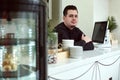 Barista at the bar behind the monitor. In front of him is a showcase with cupcakes