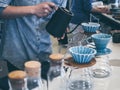 Barista in blue shirt pouring hot water from black kettle into coffee ground with filter on white counter bar Royalty Free Stock Photo