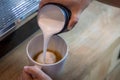 Barista in cafe or coffee bar preparing proper cappuccino pouring milk froth in a cup. Waiter hands pouring milk making cappuccino