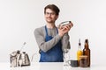 Barista, cafe worker and bartender concept. Portrait of cheerful friendly young male employee in apron mixing drinks Royalty Free Stock Photo