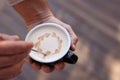 Barista creating pattern in cup of coffee on blurred background, closeup. Space for text