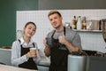 Barista man and women wearing apron holding coffee cup and thumbs up looking at camera in counter at coffee shop. Royalty Free Stock Photo