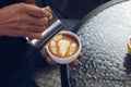 Barista pouring milk foam for making coffee latte art with pattern the leaves in a cup Royalty Free Stock Photo