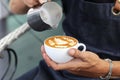 Barista pouring milk foam for making coffee latte art with pattern the leaves in a cup Royalty Free Stock Photo